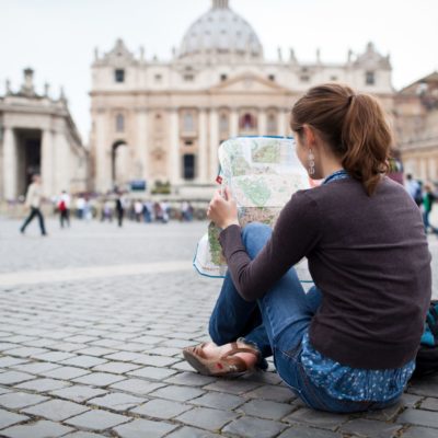 Pretty young female tourist studying a map at St. Peter's square Pretty young female tourist studying a map at St. Peter's square in the Vatican City in Rome